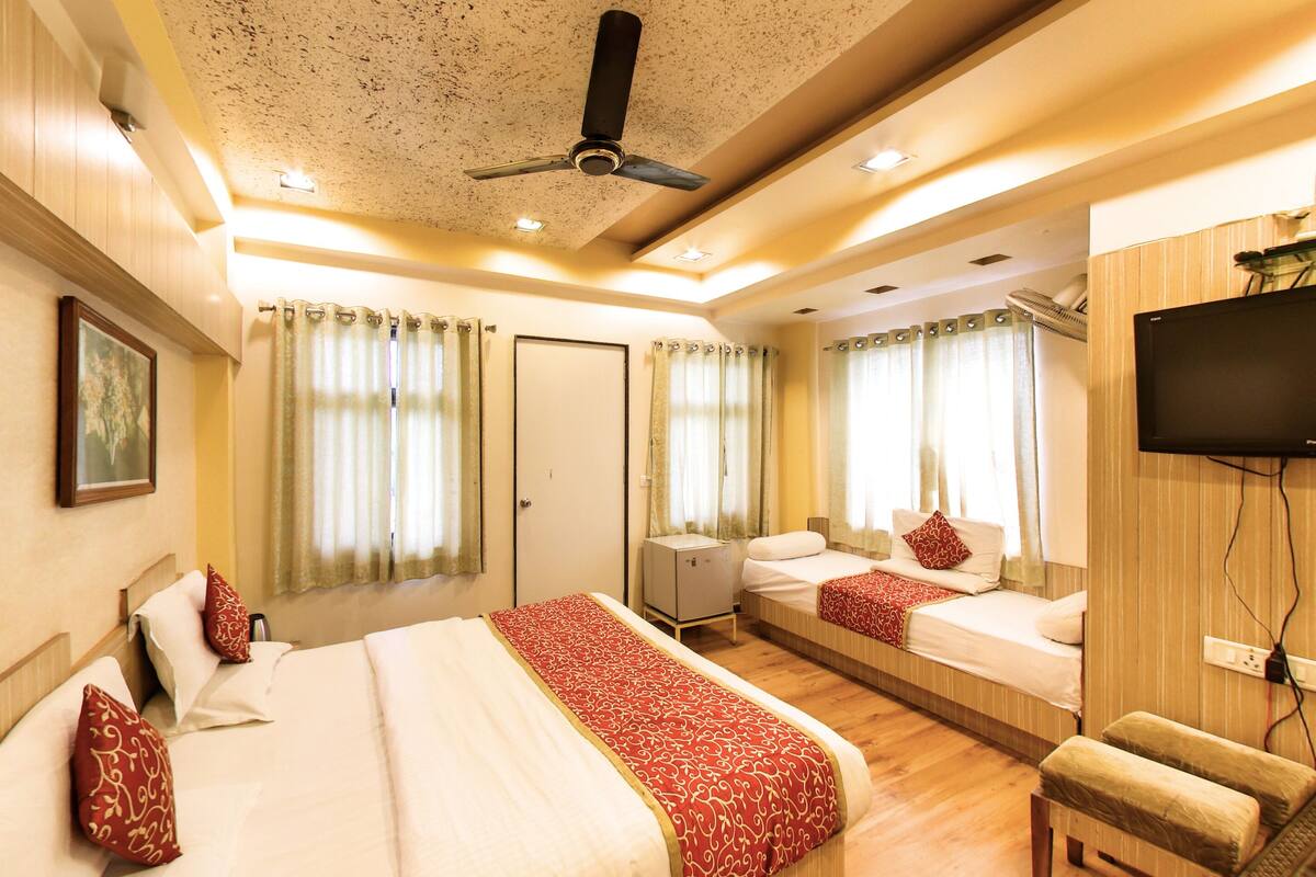 A hotel room with a large bed, two smaller beds, a TV, and a ceiling fan.