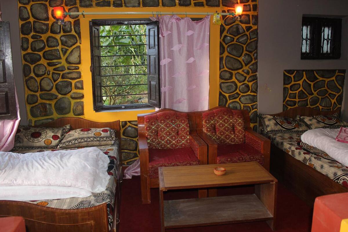 A room with a stone wall, a window with a view, two wooden beds, and a small table.