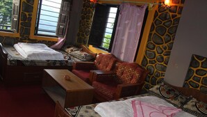 A cozy room with two beds, a sofa, and a wooden table. - Buddha Shanti Lodge Backpackers paradise (Dhulikhel)