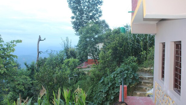 A building with a red roof, surrounded by lush greenery and a view of a distant landscape. - Buddha Shanti Lodge Backpackers paradise (Dhulikhel)