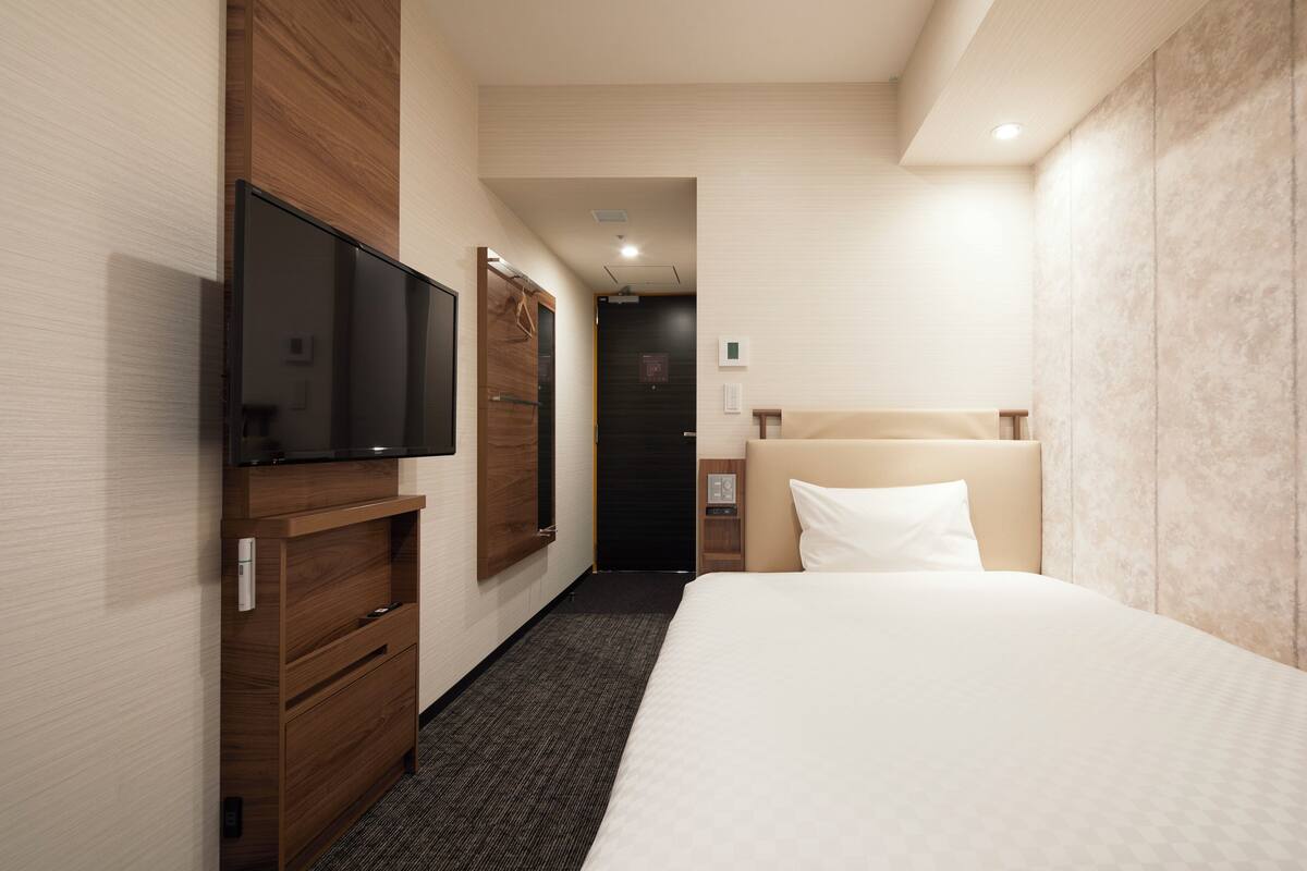 Una habitación de hotel con cama, televisión, armario y puerta que da a otra estancia.