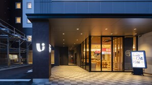 Un edificio moderno con suelo a cuadros, un llamativo letrero iluminado con la letra 'U' y una entrada de vidrio que da a un restaurante.