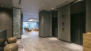 Un vestíbulo moderno con una recepción, dos ascensores y un área de estar con vistas al exterior.
