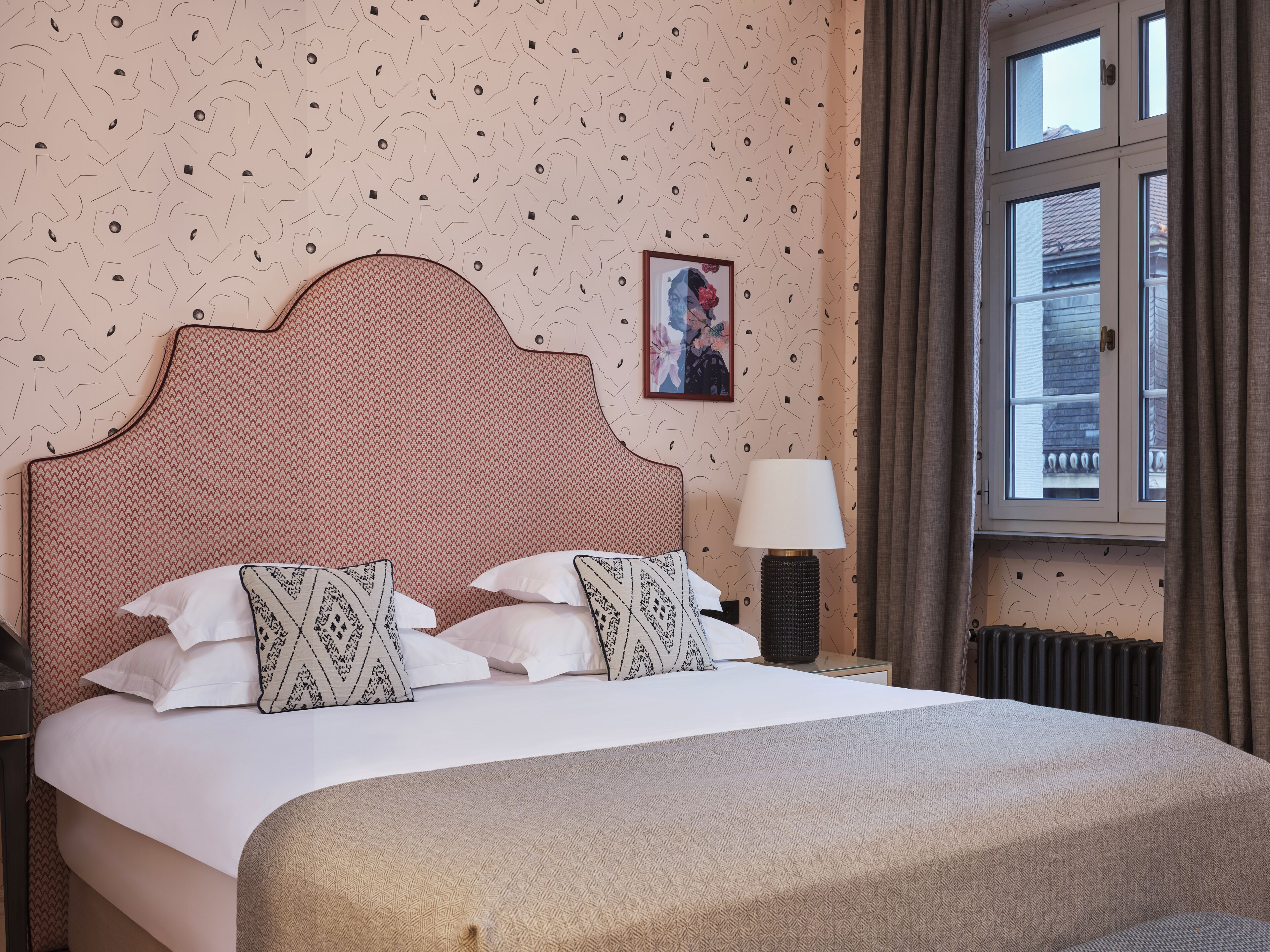 Una cama bien tendida con almohadones estampados, cabecera y lámpara de noche.