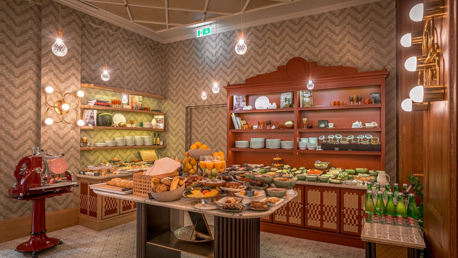 A buffet setup with various food items and beverages, wooden shelves with plates and glasses, and hanging light fixtures.