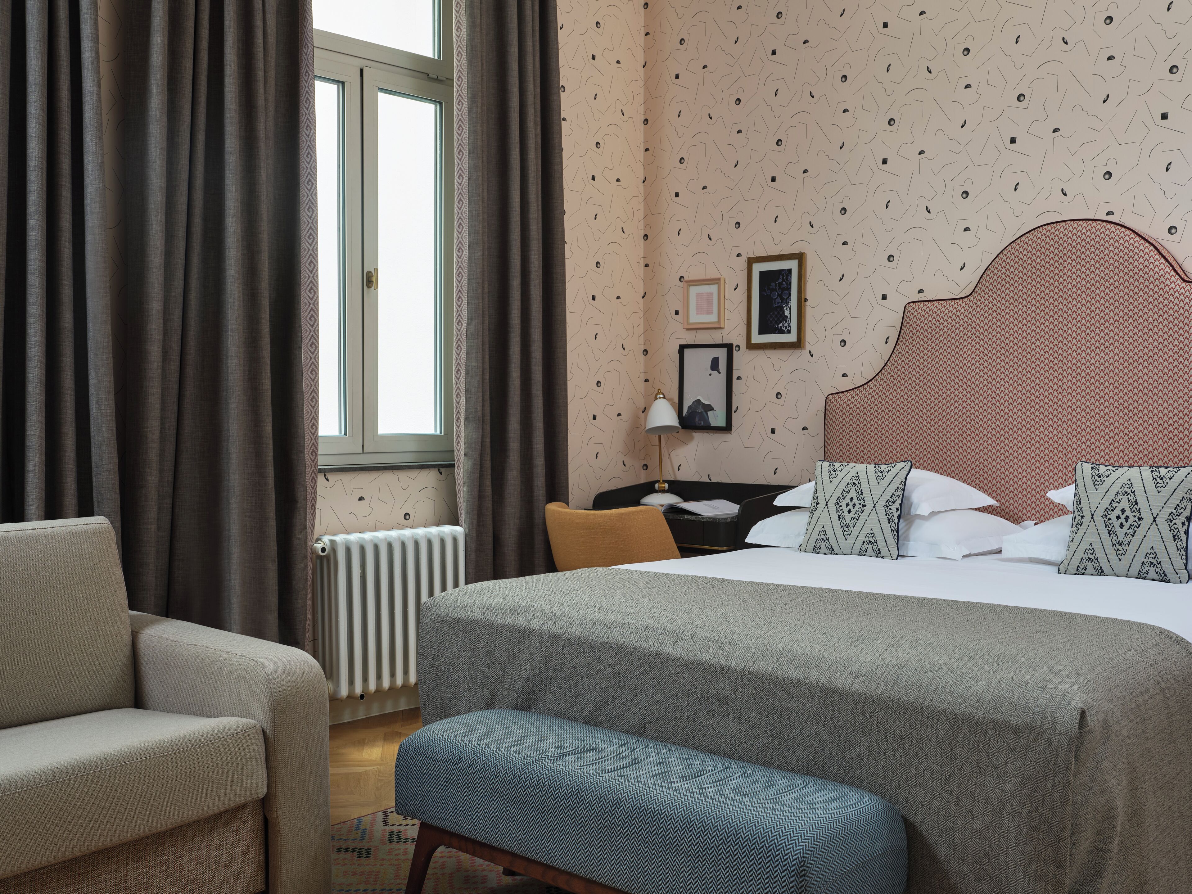 A hotel room with a large bed, a chair, a desk, and a window with curtains.