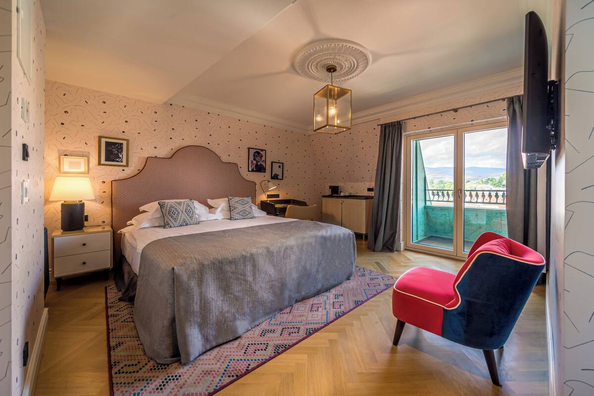 Ein Hotelzimmer mit einem großen Bett, einem Schreibtisch, einem Stuhl, einem Fernseher und einem Balkon mit Blick.