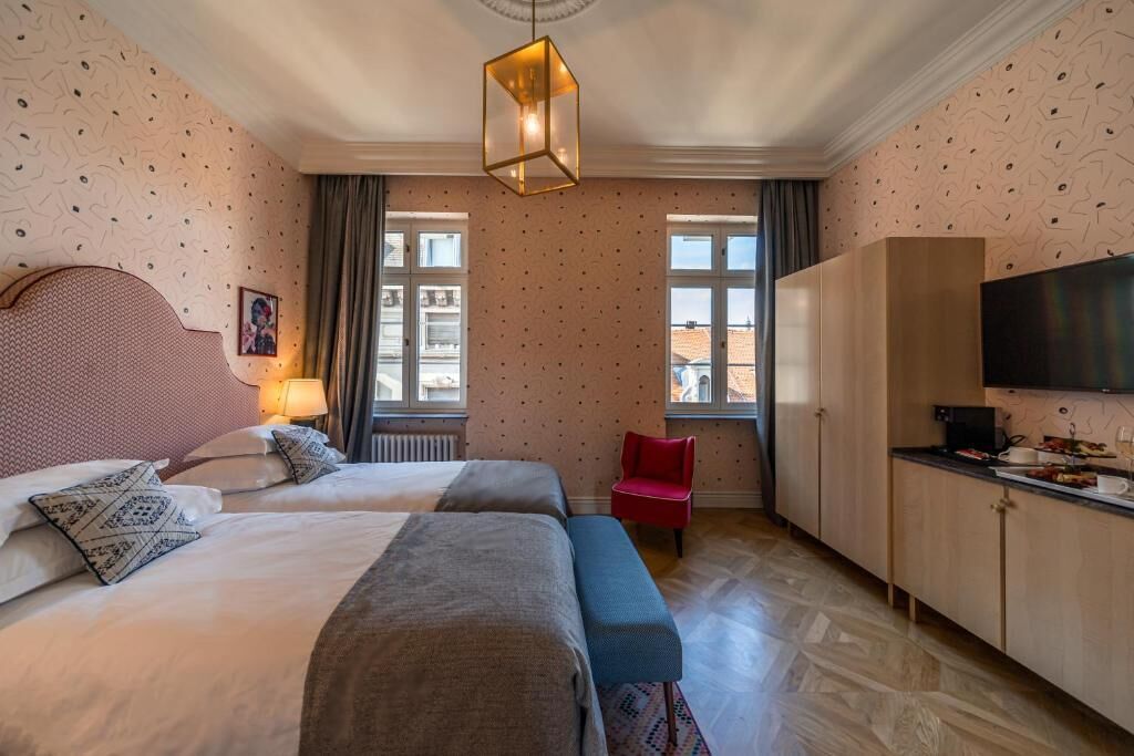 A hotel room with two beds, a red chair, a TV, and a large window.