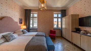 A hotel room with two beds, a red chair, a TV, and a large window.