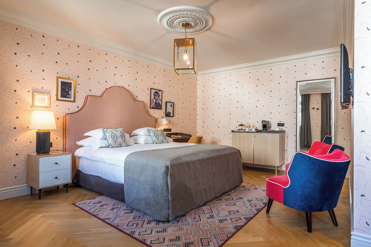 Ein Schlafzimmer mit einem Bett, Nachttischen, einem Sessel, einem Schreibtisch und einem Spiegel.