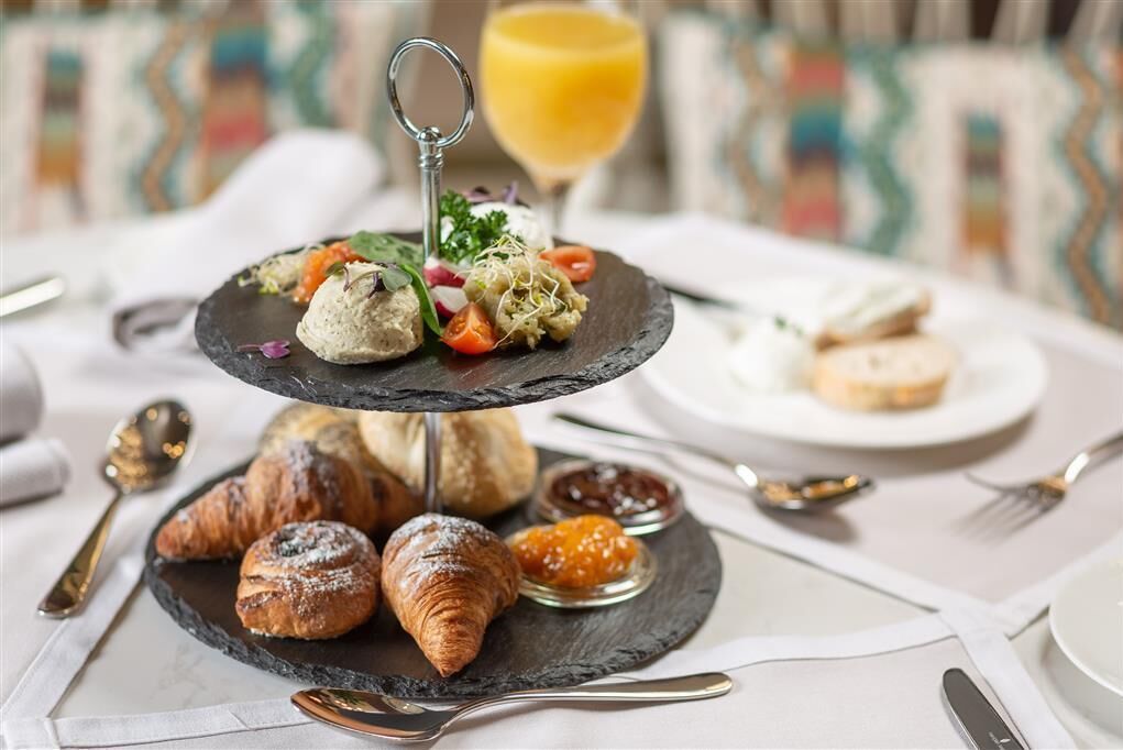 A three-tiered serving board with pastries, croissants, and a glass of orange juice.