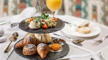 A three-tiered serving board with pastries, croissants, and a glass of orange juice.