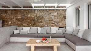 Un salon moderne avec un mur en pierre, un canapé d’angle et une table basse en bois sur laquelle repose une tranche de pastèque.
