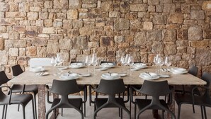 Une table à manger dressée avec des assiettes, des verres et des couverts, le tout placé devant un mur de pierre.