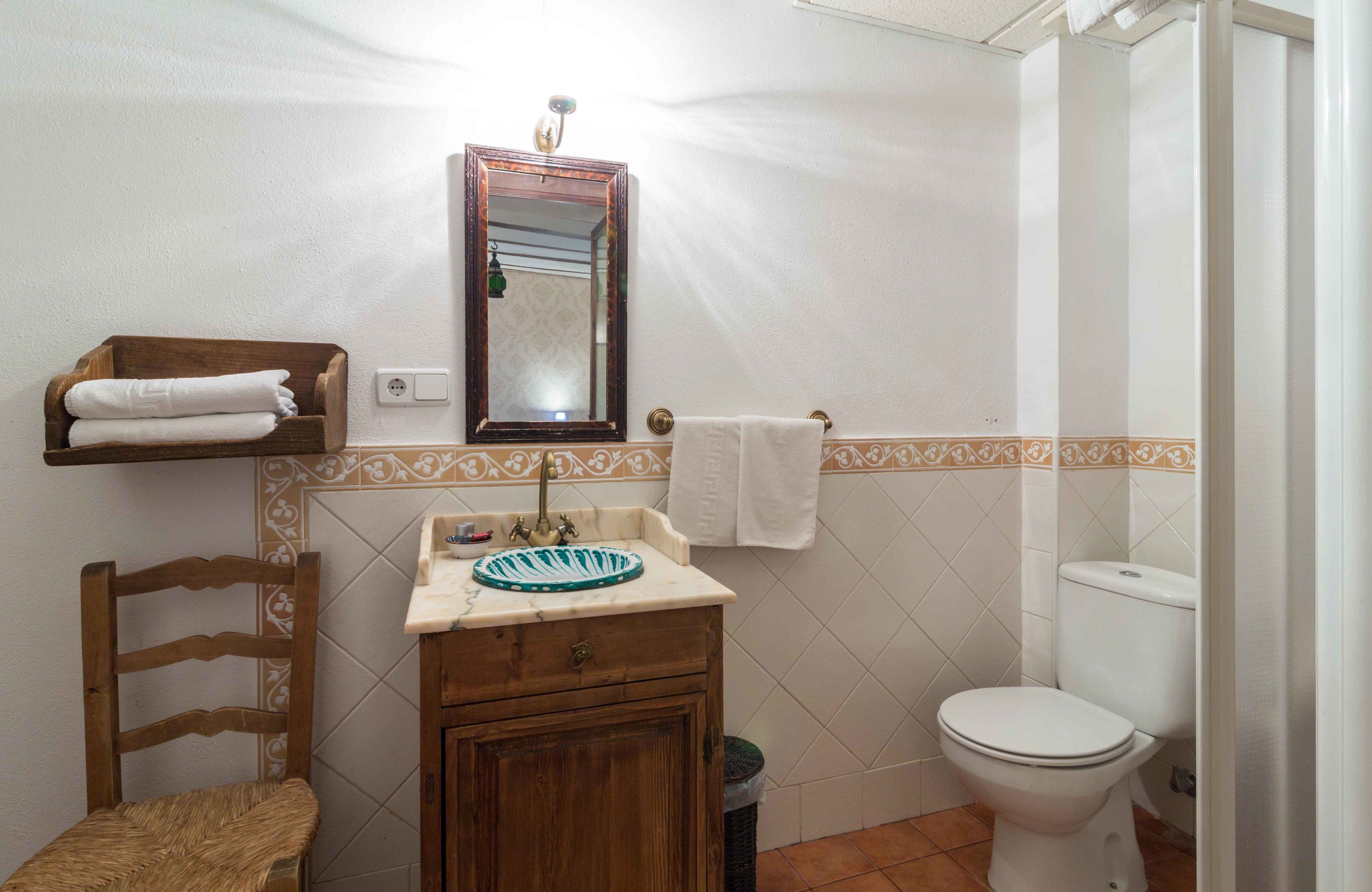 Ein kleines Badezimmer mit einem Holzkosmetikschrank, einem Spiegel, einer Toilette und einem Stuhl.