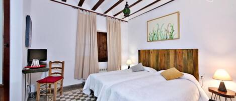 Una habitación con dos camas, un escritorio con silla, un televisor y una lámpara.