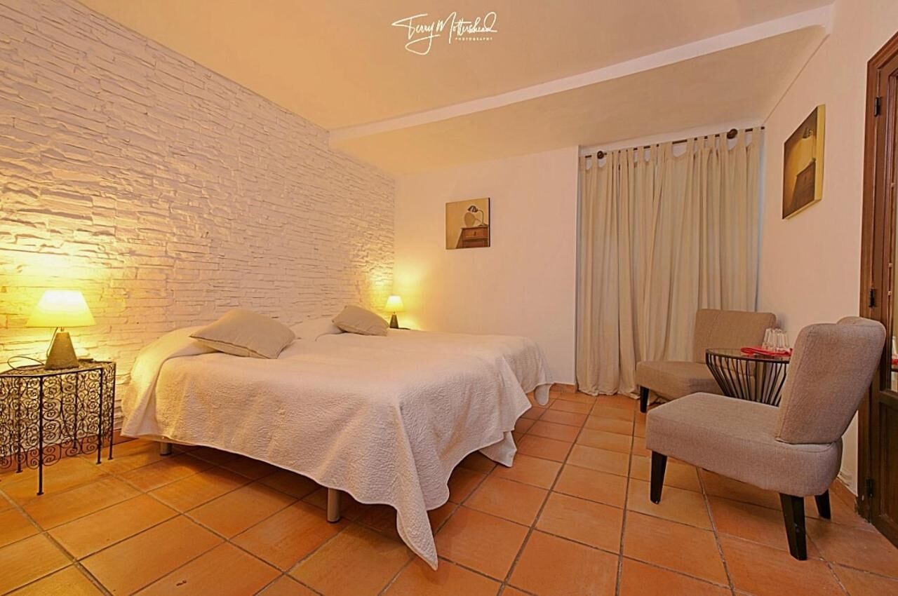 A bedroom with two beds, a chair, a small table, and a wall with a textured design.