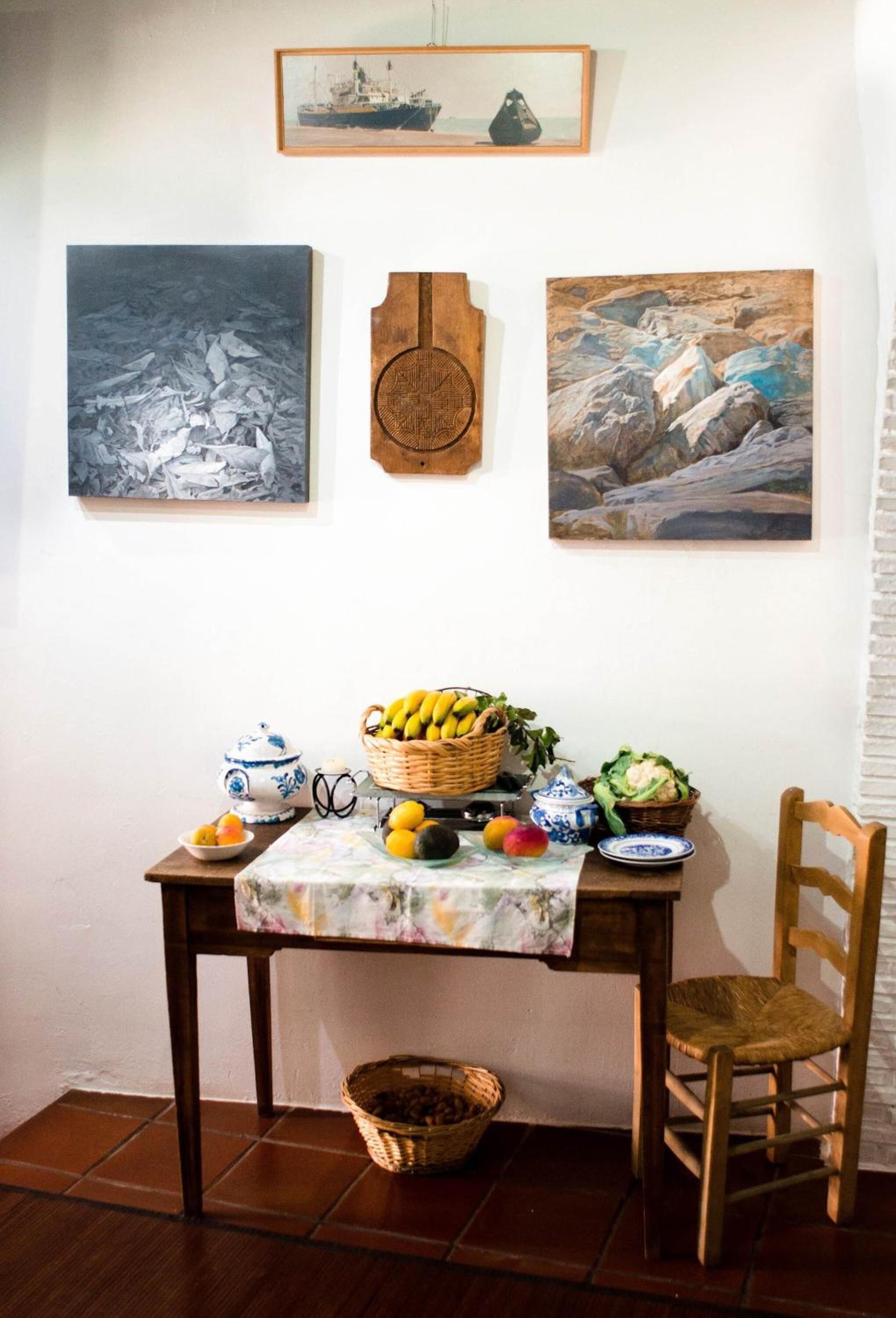 A dining table with a floral tablecloth, a wooden chair, and a basket of fruits.