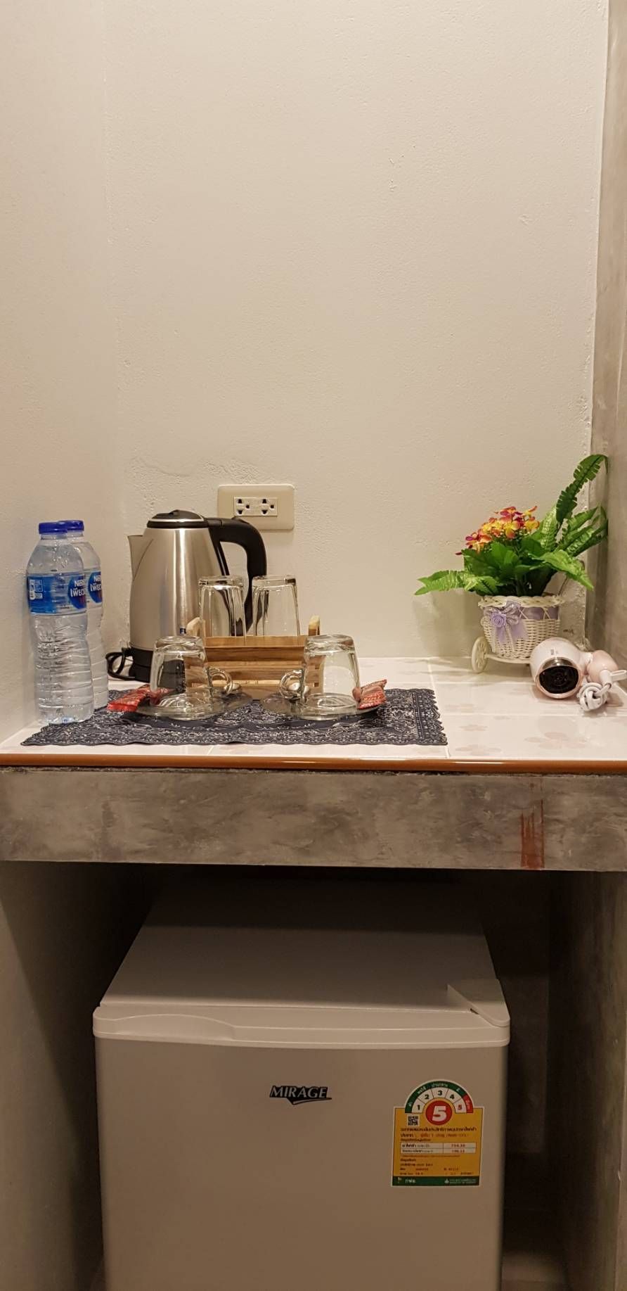 A kitchenette with a coffee maker, a kettle, a water bottle, and a small potted plant.