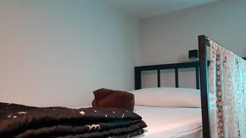 Una cama individual con un edredón oscuro y una almohada marrón, un cabecero de madera con motivos florales, y una pared blanca lisa al fondo.