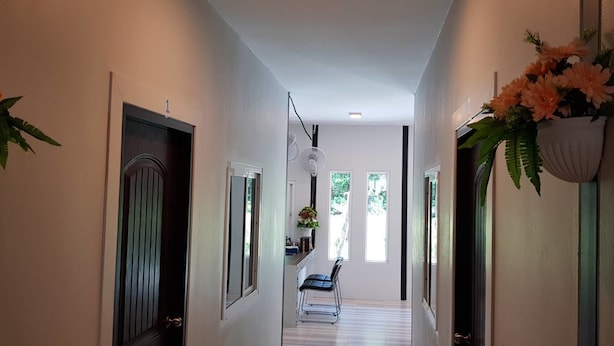 A hallway with a door on the left, a fan on the right, and a chair in the center. - Nest  Hostel Lipe (Koh Lipe)