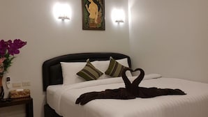 A hotel room with a bed, a nightstand, a vase with flowers, a painting on the wall, and an air conditioning unit. - Nest  Hostel Lipe (Koh Lipe)