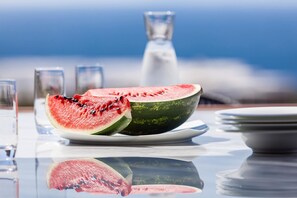A table with a watermelon and a glass of water, reflecting on a glass surface.