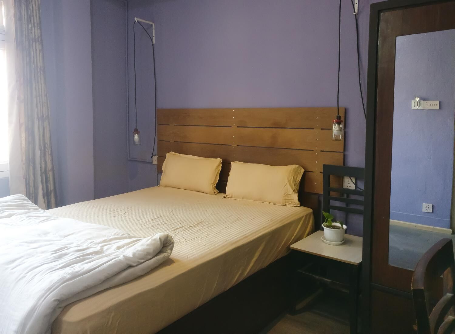 A bedroom with a bed, a wooden headboard, a bedside table with a plant, and a chair.