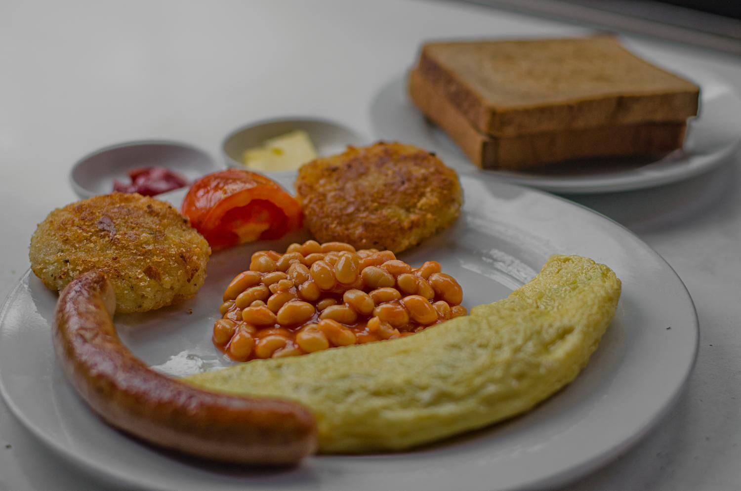 Une assiette comprenant une saucisse, des aliments frits, des haricots, une tranche de pain grillé et un œuf dur.