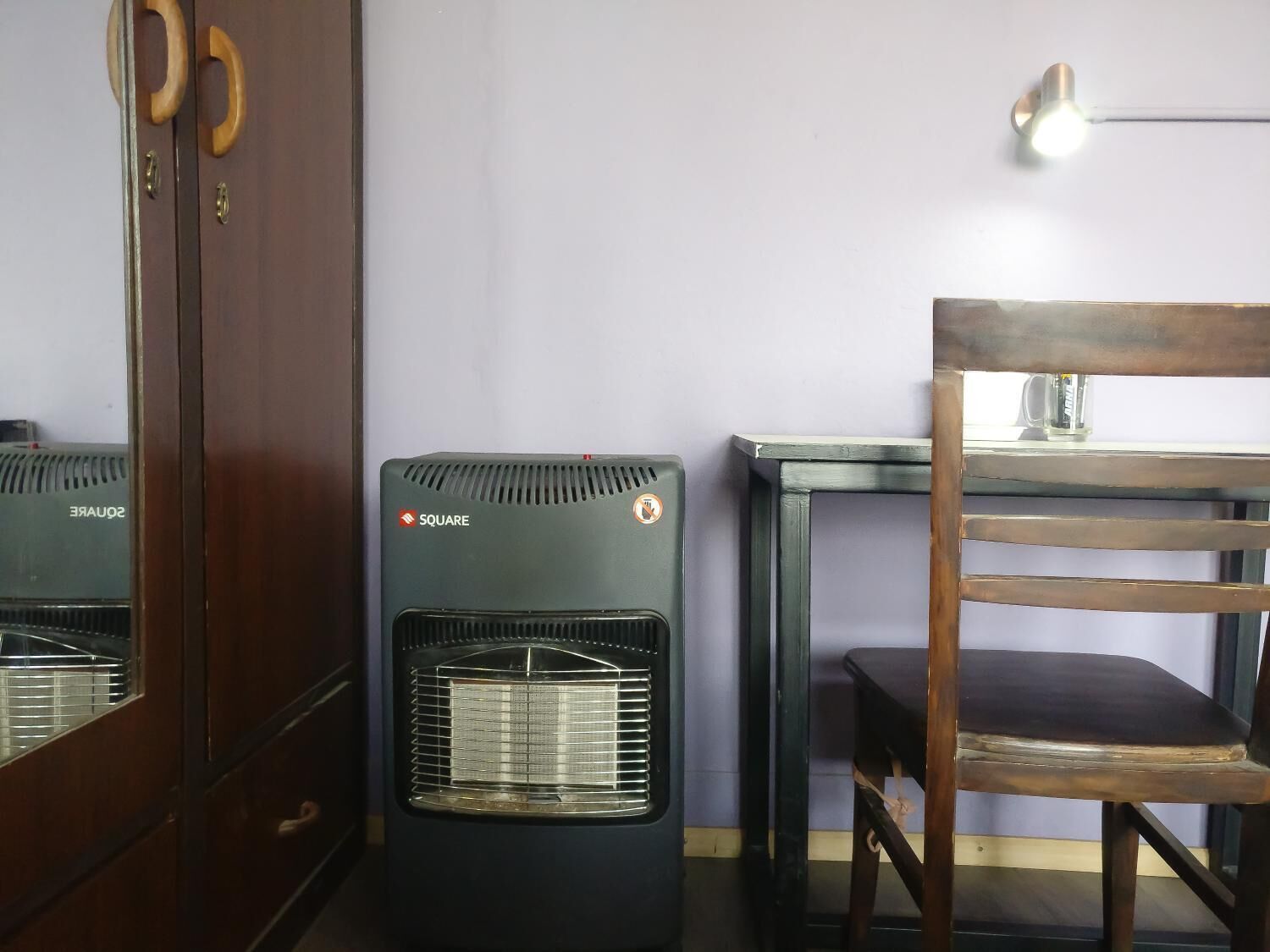 A room with a black heater labeled 'SQUARE', a wooden chair, and a small table with a lamp.