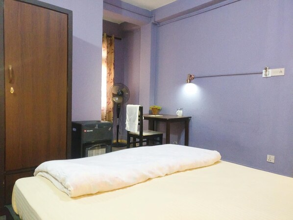 A bedroom with a bed, a desk with a chair, a fan, and a wall-mounted light fixture. - Sun Apartment & Guest House (Lalitpur)