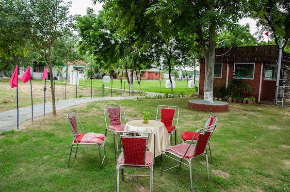 An outdoor seating area with a round table and red chairs, surrounded by trees and a building in the background.