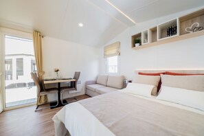 Quarto de hotel moderno com uma cama grande, uma escrivaninha e um sofá. Há prateleiras com livros e uma planta.