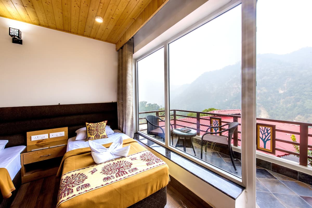 Ein Hotelzimmer mit großem Fenster und Bergblick, einem Bett mit dekorativem Kopfteil, einem kleinen Tisch und einem Stuhl auf dem Balkon.
