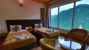 A hotel room with two beds, a wicker chair, a small table, and a large window offering a mountain view. - Veda5 Ayurveda And Yoga Retreat (Yamkeshwar)