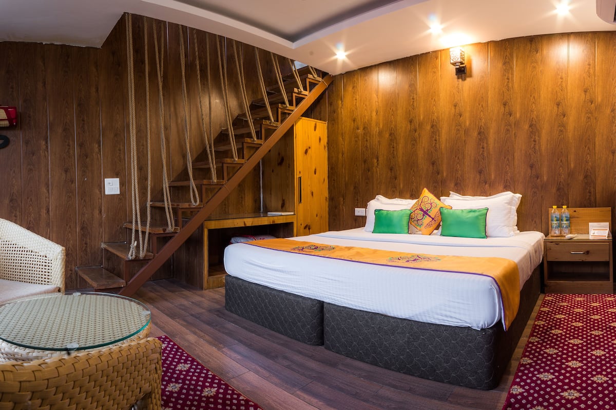 Ein Schlafzimmer mit einer Holztreppe, einem Bett mit vielen Kissen, einem Nachttisch mit Wasserflaschen und einem Korbstuhl.