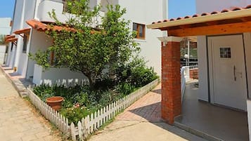 A modern multi-story building with a white facade, a small balcony, and a brick column.