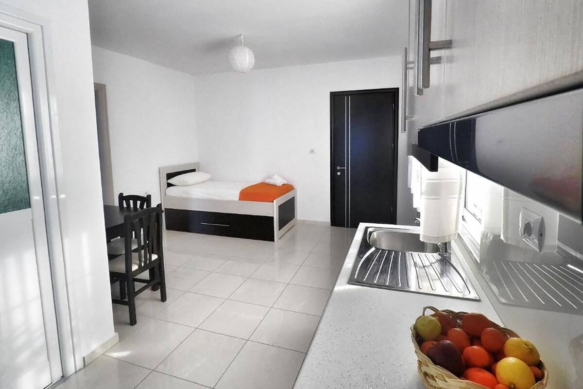 A modern, compact room with a bed, a dining table, and a kitchen area.