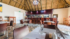Un restaurant doté d’un toit de chaume, de tables et de chaises en bois, et d’un espace bar.