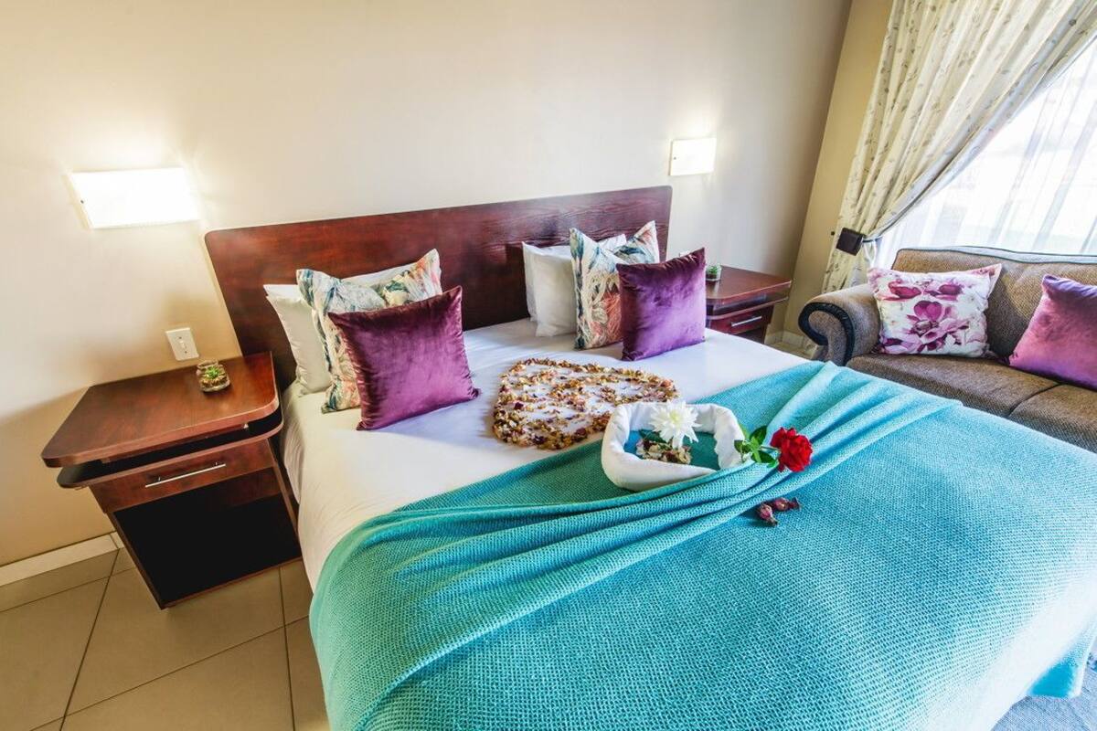 A hotel room with a bed, a nightstand, a sofa, and a window with curtains.