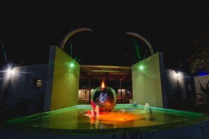 A nighttime view of a modern building with a spherical water feature in the center, surrounded by illuminated arches.