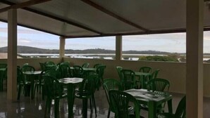 A covered outdoor seating area with green plastic chairs and tables, overlooking a body of water and distant hills. - Pousada Mar do Sonho (Ipojuca)