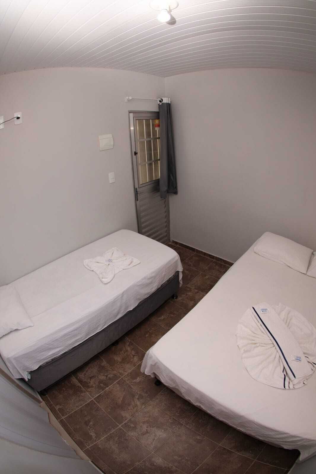 A small, clean room with two single beds, a ceiling fan, and a window with a curtain.