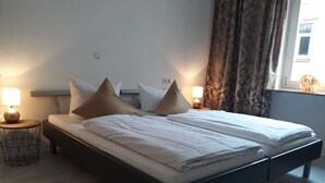 A neatly made bed with white linens, two bedside tables with lamps, and a window with curtains. - Ricks City Hotel 2 (Trier)