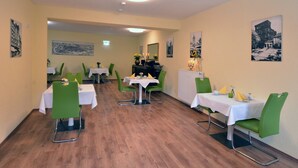 A dining area with tables and chairs, a radiator, and framed pictures on the walls. - Ricks City Hotel 2 (Trier)