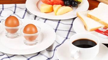 Un desayuno con una fuente de fruta, huevos, tostadas y café sobre un mantel a cuadros.