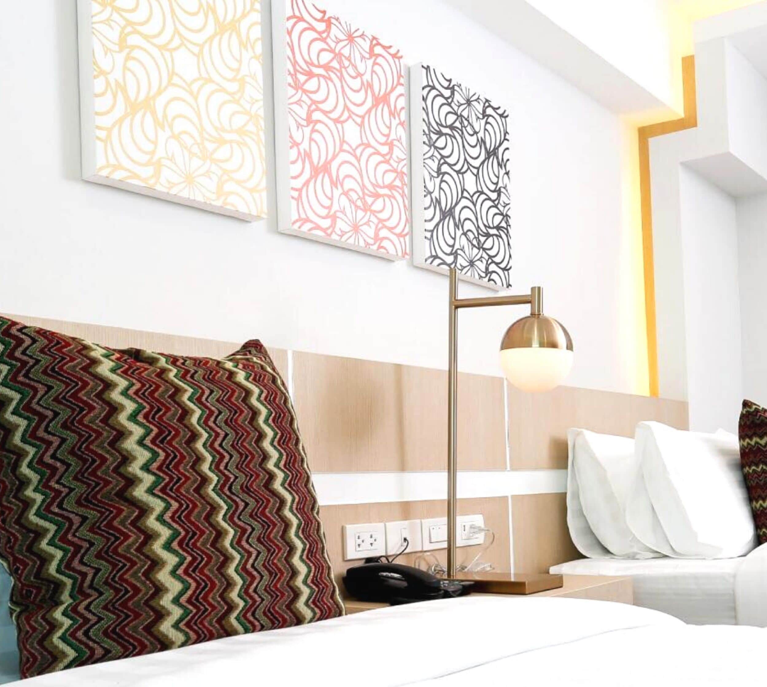 A hotel room with a bed, a nightstand, a lamp, and three patterned wall art pieces.