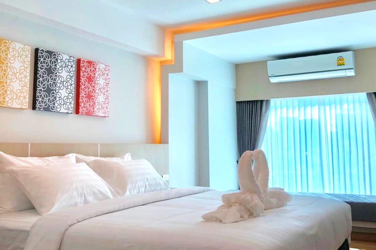 Habitación de hotel con una cama bien hecha, aire acondicionado de pared y una ventana con cortinas.