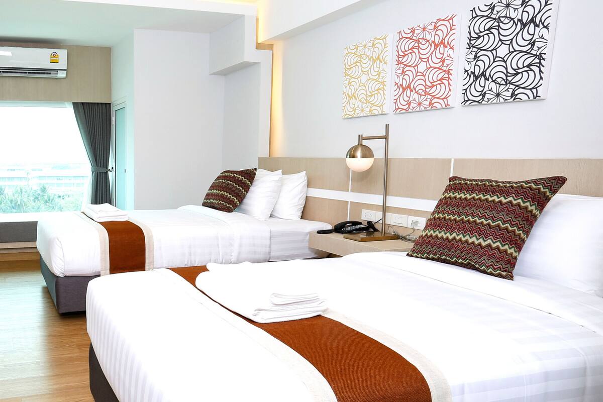Una habitación de hotel con dos camas, un escritorio, una lámpara y una ventana con cortinas.