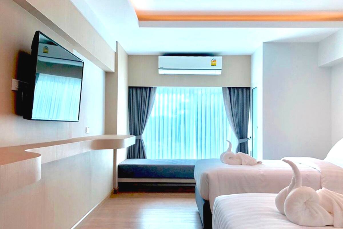 Habitación de hotel con una cama, televisor montado en la pared, aire acondicionado y ventana con cortinas.